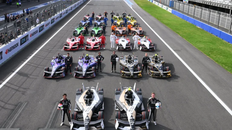 Formula E race cars line up on the grid with drivers standing beside their vehicles