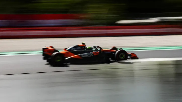 A Mclaren F 1 car on track with a blurred background indicating the vehicle is traveling at high speed
