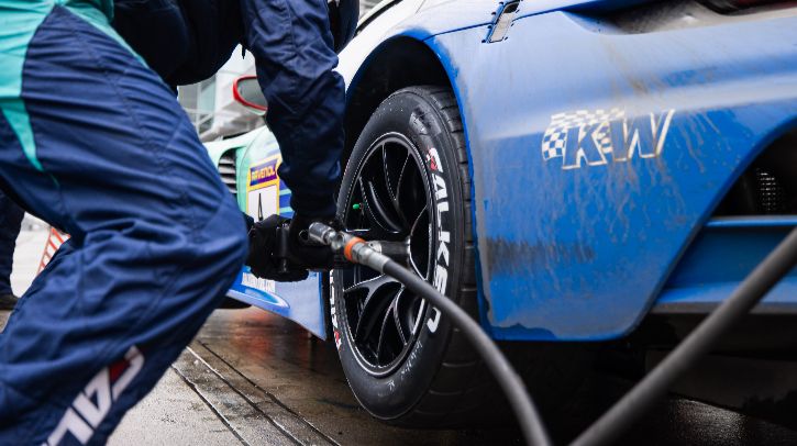 Falken tires with Sensing Core technology on a dark blue race car during an NLS race, with a team member in blue pitstop clothing tightening wheel nuts