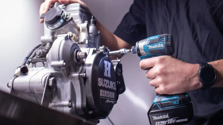 An engineer uses a power tool on a small motorbike engine.